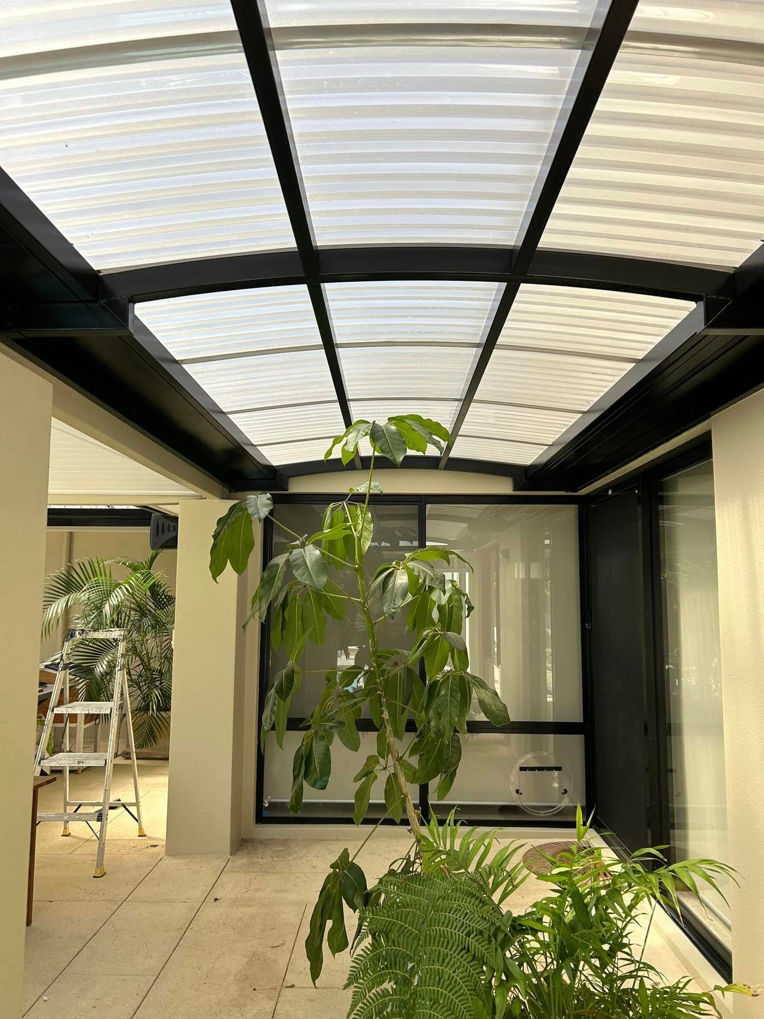 Indoor courtyard with potted plants under a curved glass roof and black metal frame.