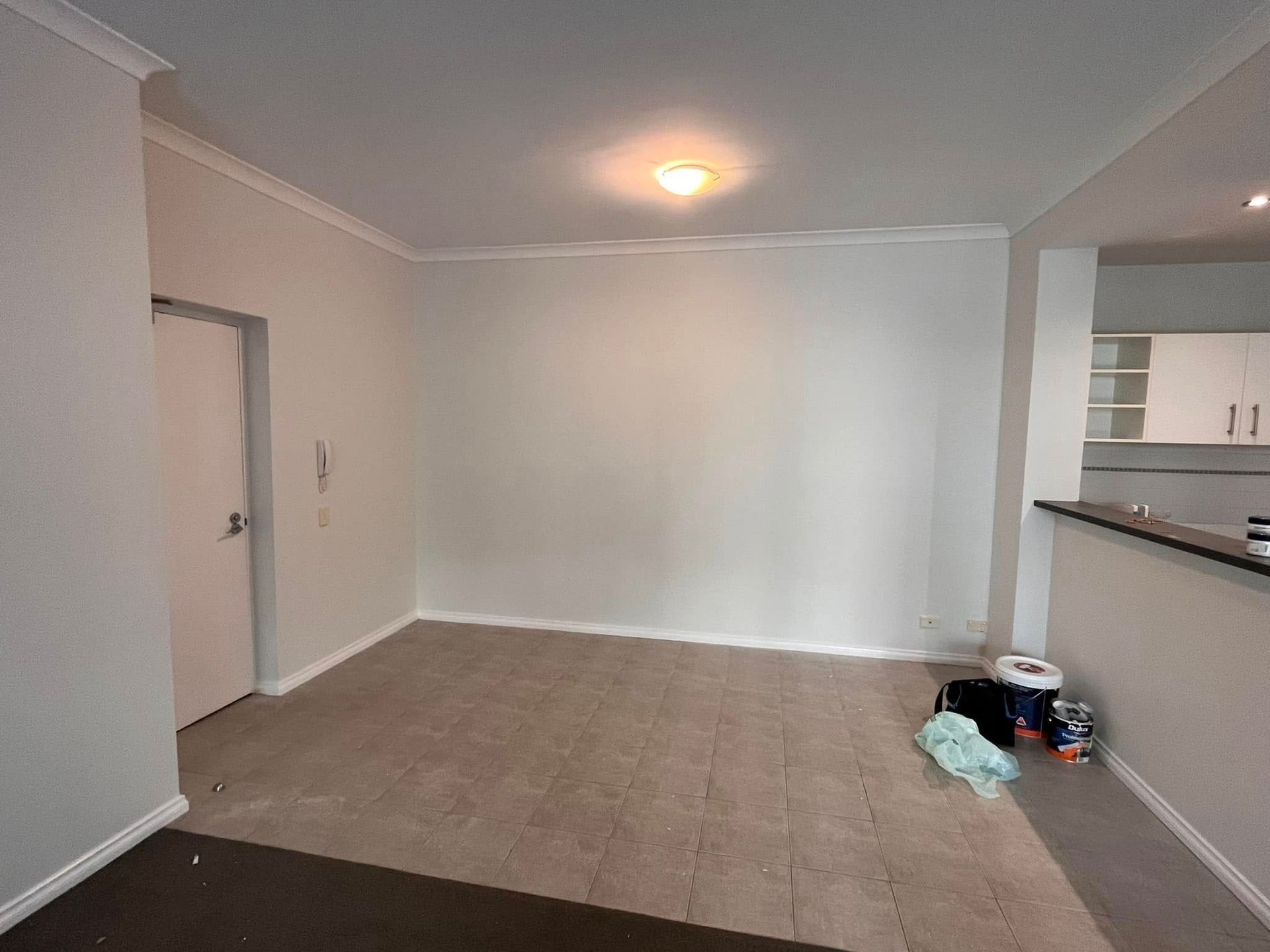 Empty carpeted living room with beige walls, ceiling light, and a kitchen pass-through on the right