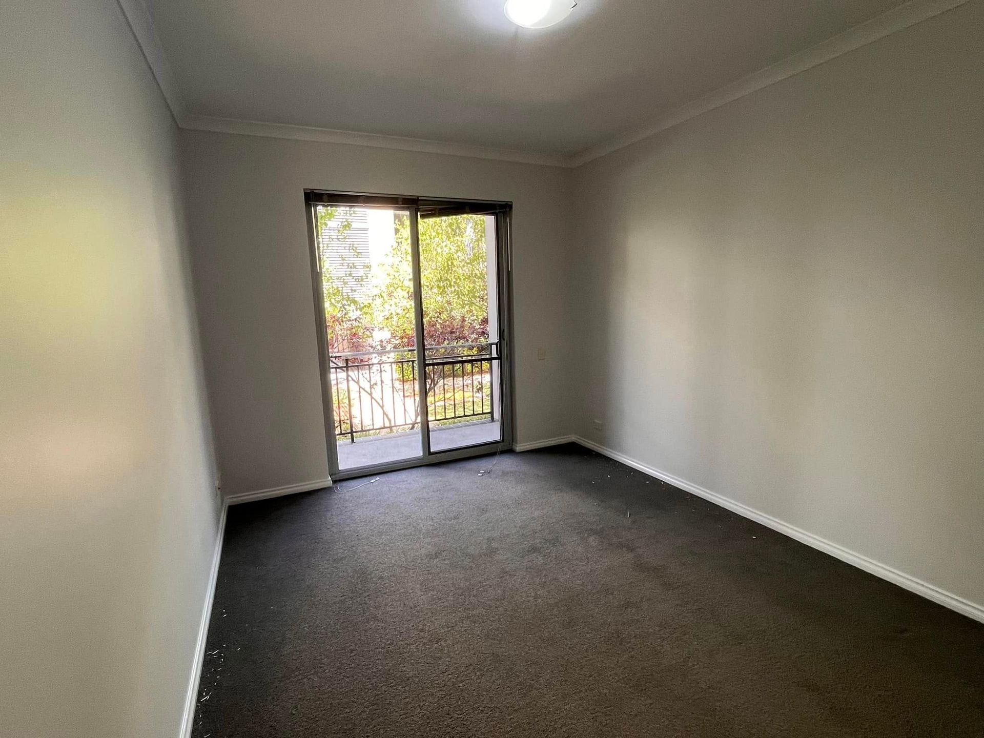 Empty carpeted room with white walls and a sliding glass door opening to a balcony.