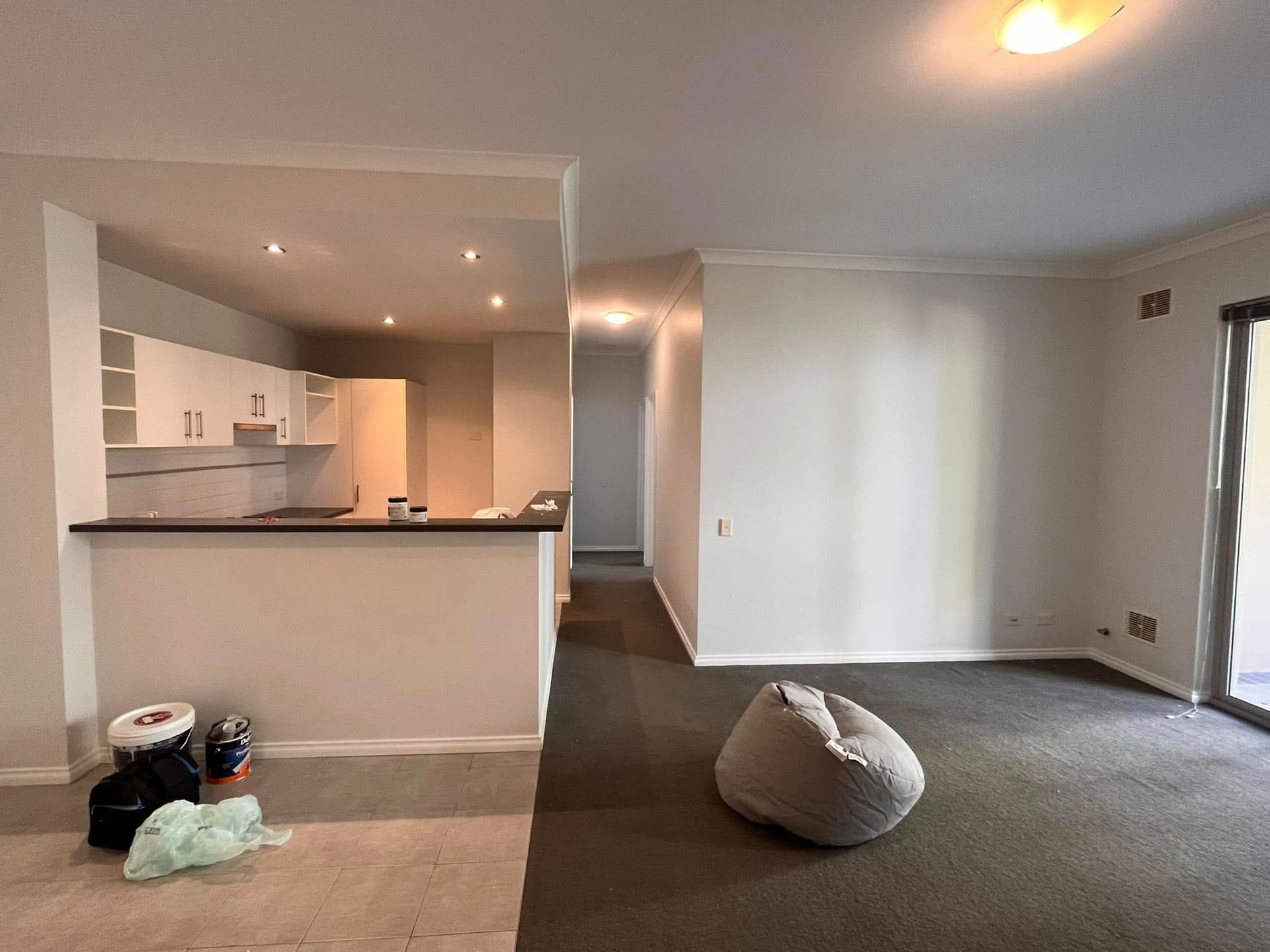 Empty living room with carpet, beanbag chair, and open kitchen pass-through.