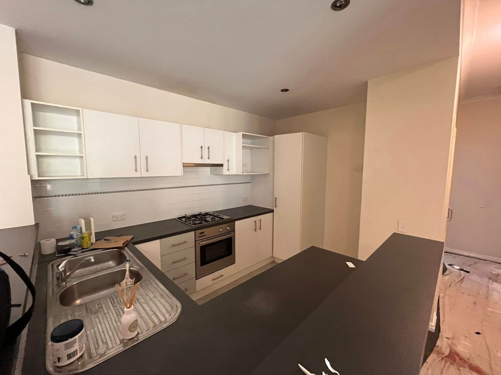 Small modern kitchen with white cabinets, black countertop, oven, sink, and open shelving.