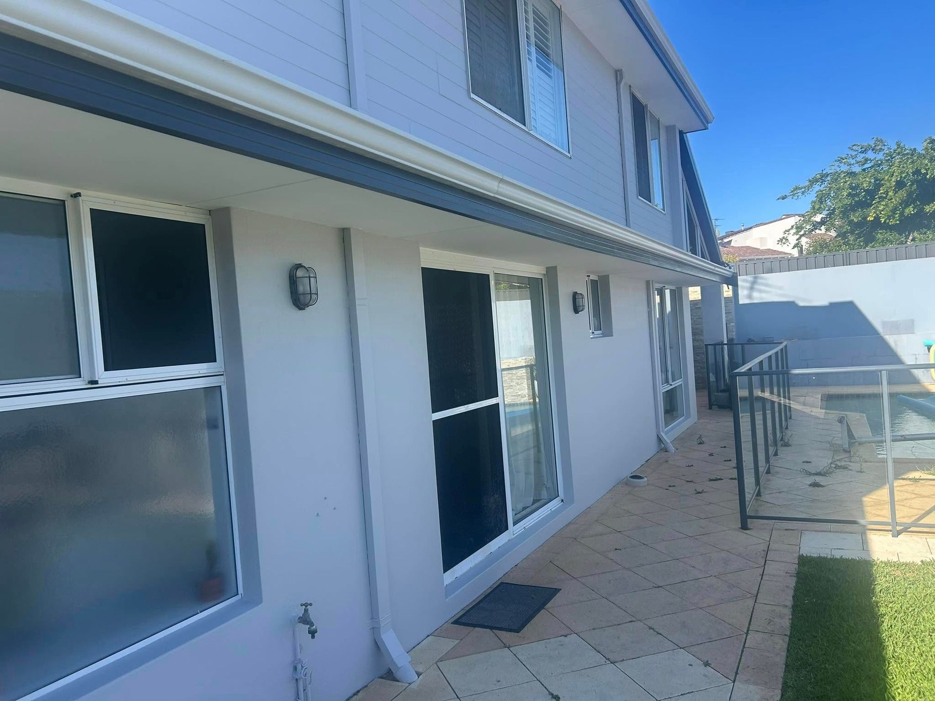 Patio beside a white two-story house with sliding glass doors, windows, and a fenced grassy yard.