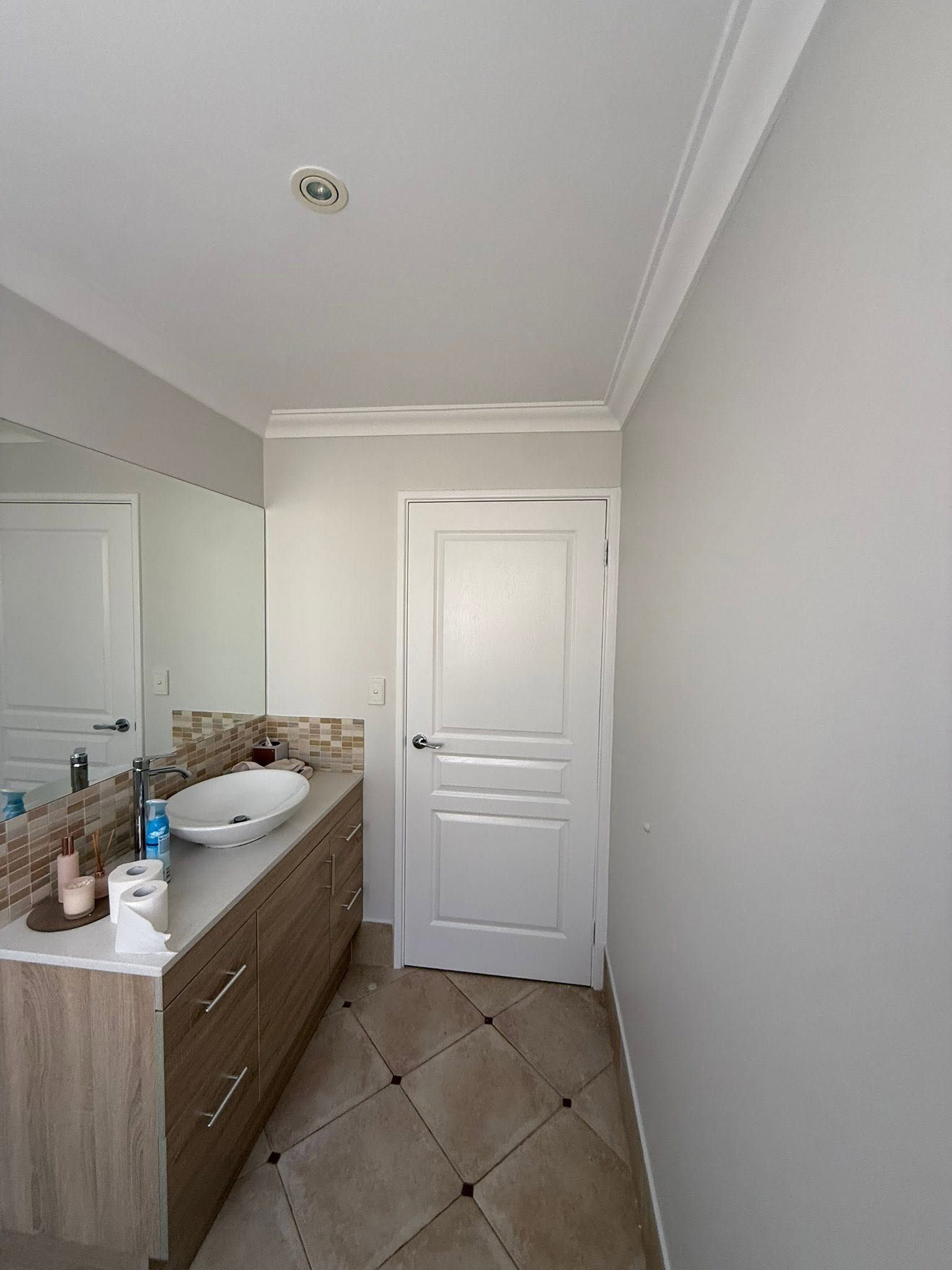 Narrow bathroom with white door, tiled floor, sink vanity, and large wall mirror.