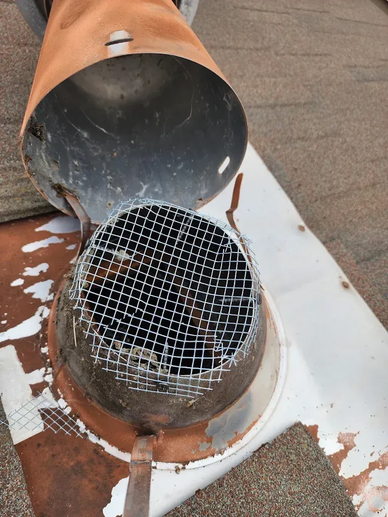 Open metal pipe with hinged cap and wire mesh cover on a rusted white surface
