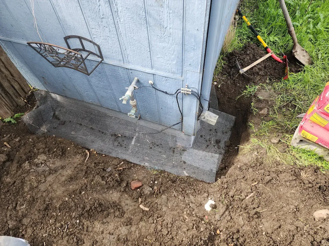 Dirt beside a blue house wall with exposed wiring and a small concrete foundation corner.