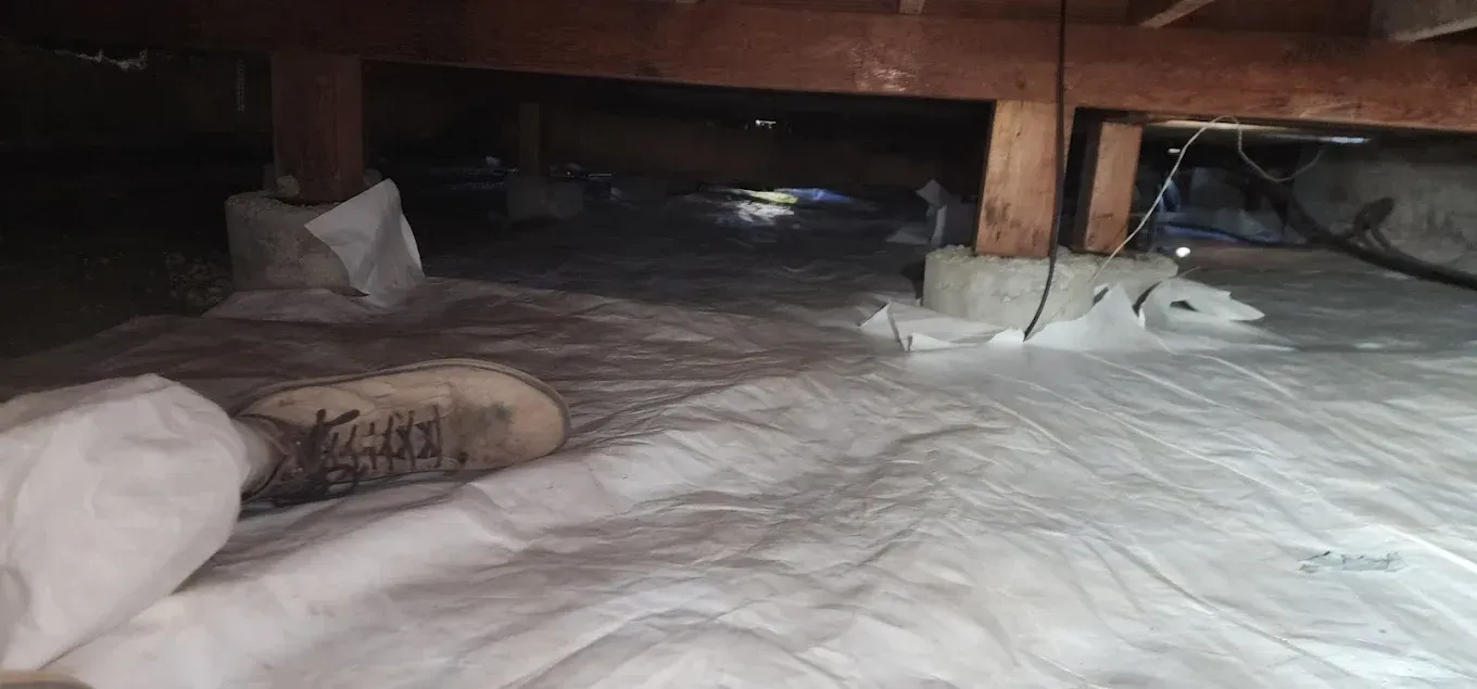 Insulated crawlspace under wooden beams with plastic sheeting and a small bag on the floor