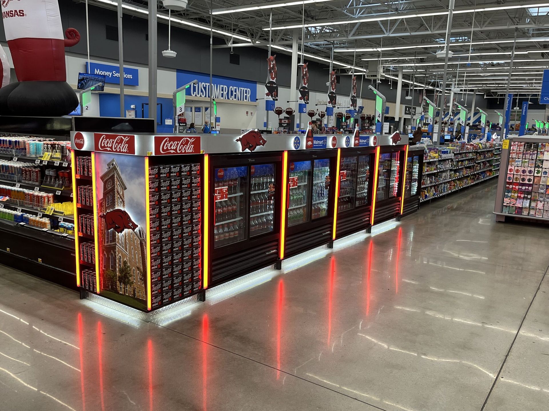 A long row of Coca-Cola coolers in a bright supermarket aisle with reflective polished floors.
