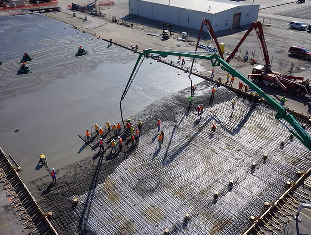 Workers pour concrete on a large construction site with a boom pump and rebar grid.