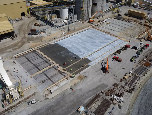 Aerial view of a large construction site with a concrete slab, machinery, materials, and parked vehicles.