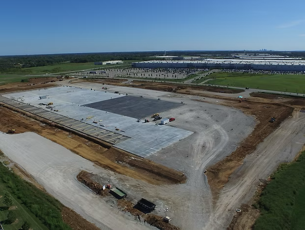 Aerial view of a large construction site with graded soil and a concrete foundation slab.