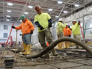 Workers in hard hats and safety gear pouring concrete at a construction site