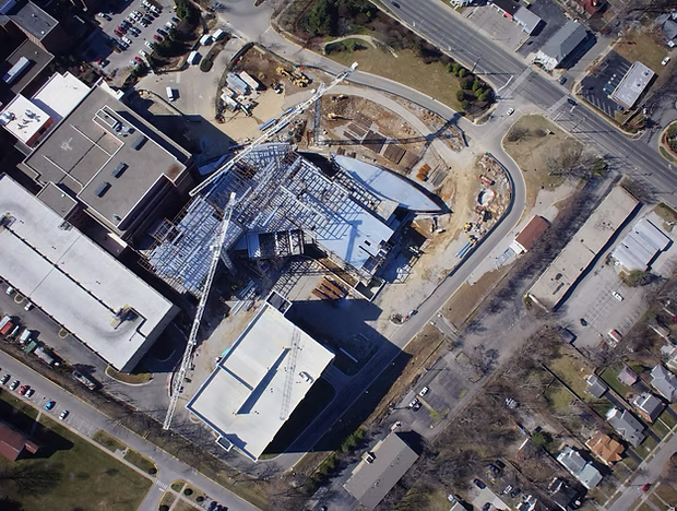Aerial view of a construction site with a partially built steel frame beside surrounding roads and buildings