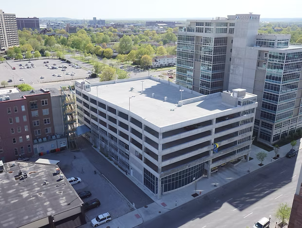 Aerial view of a city parking garage beside office buildings and leafy trees.