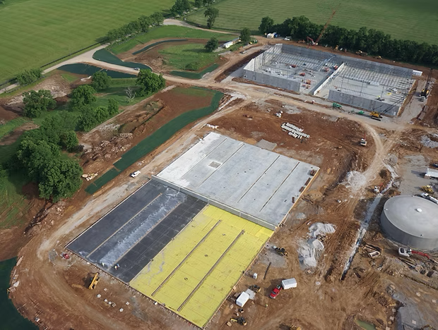 Aerial view of a construction site with concrete slabs, dirt roads, and nearby green fields