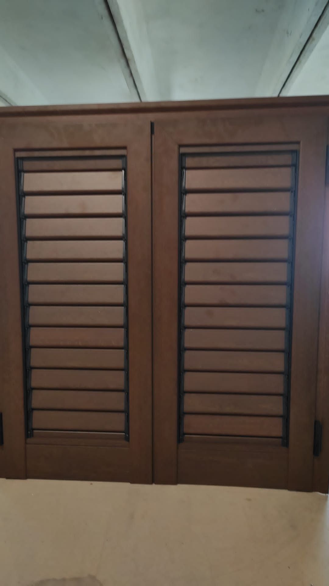 Persiane marroni in legno a lamelle su una parete sotto un soffitto bianco