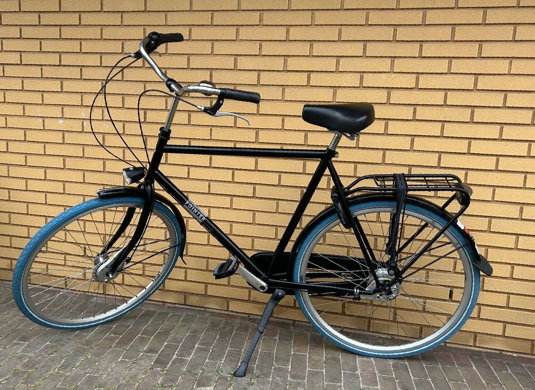 Een zwarte fiets met blauwe banden staat geparkeerd tegen een lichtstenen muur.