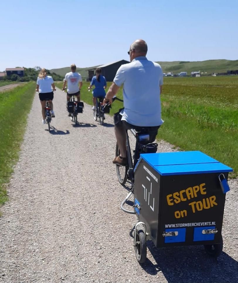 Een groep mensen fietst over een grindpad, gevolgd door een aanhanger met