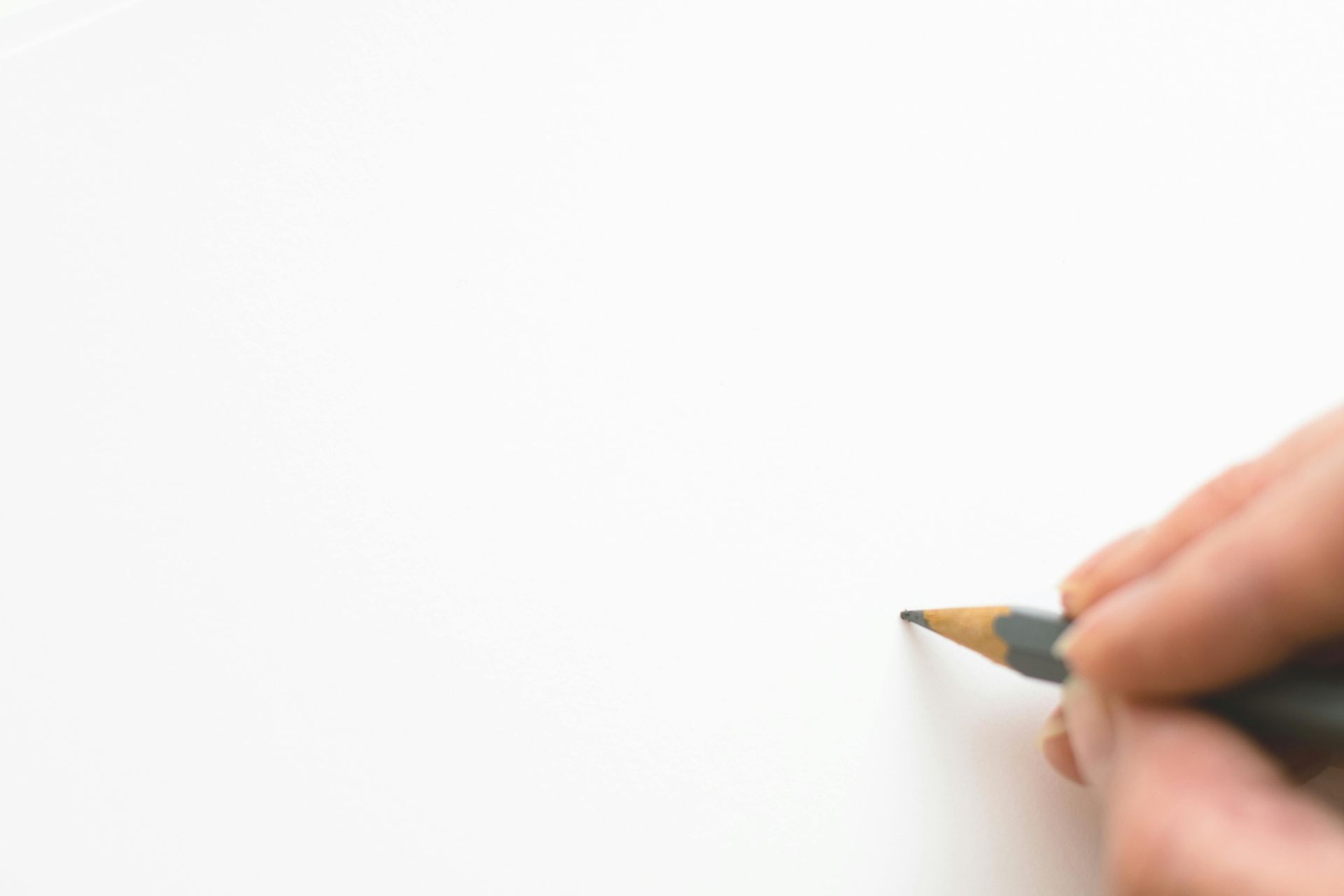 Een hand houdt een potlood vast, klaar om te tekenen op een blanco wit vel papier.