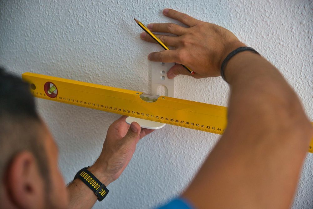 A man is measuring a wall with a yellow level and a pencil.