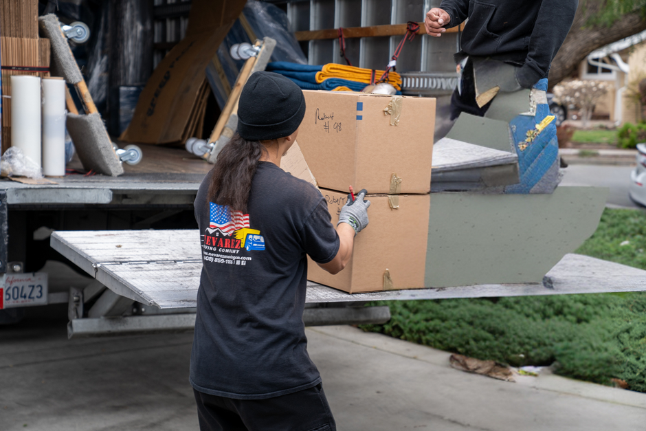 A man in a black jacket with the word pack on the back A man is loading boxes into a truck.