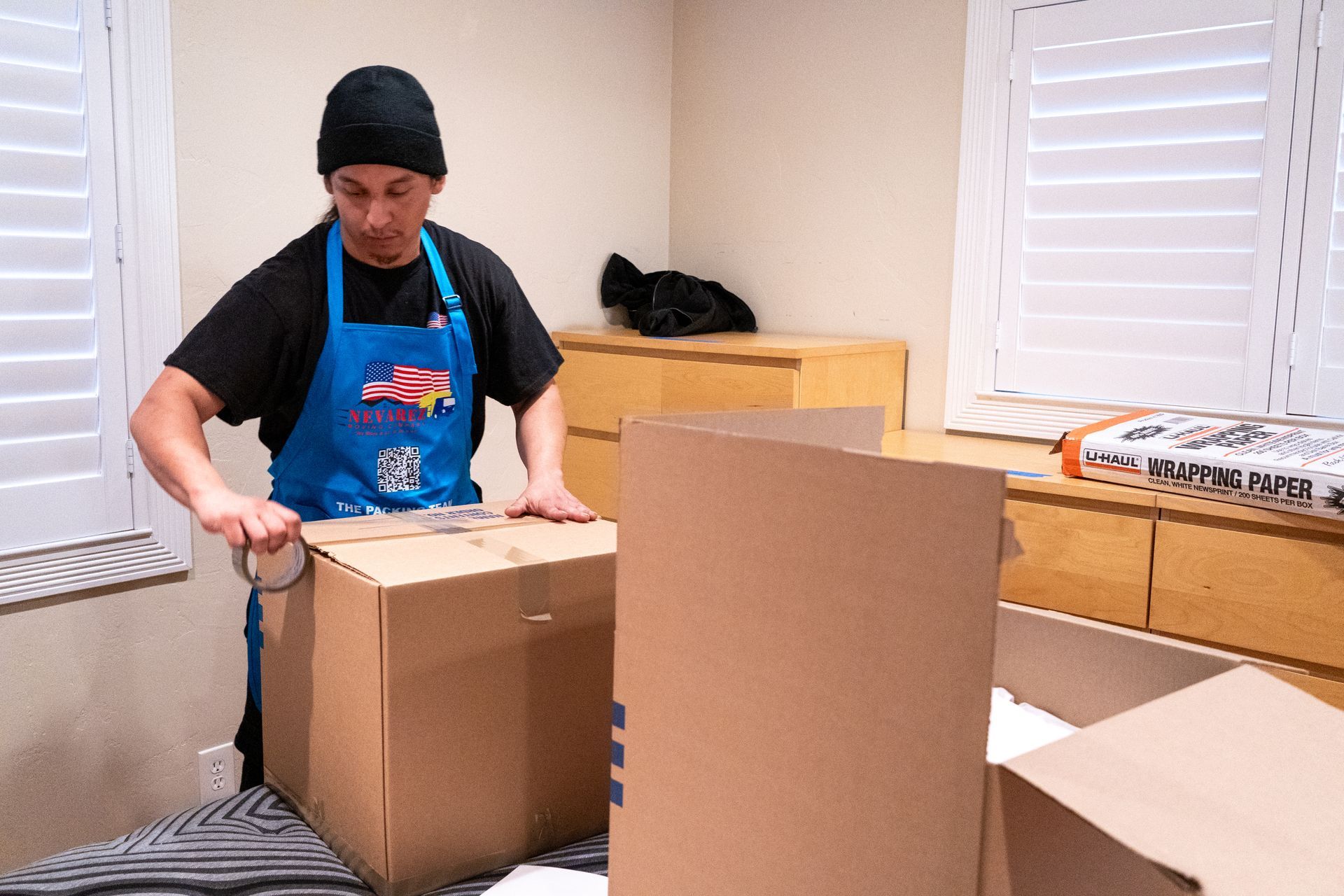 A man in an apron is wrapping a cardboard box with tape.
