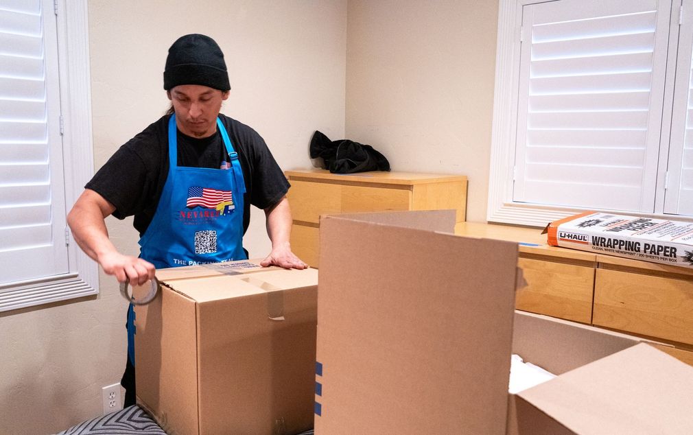 A man in a blue apron is wrapping a cardboard box with tape.
