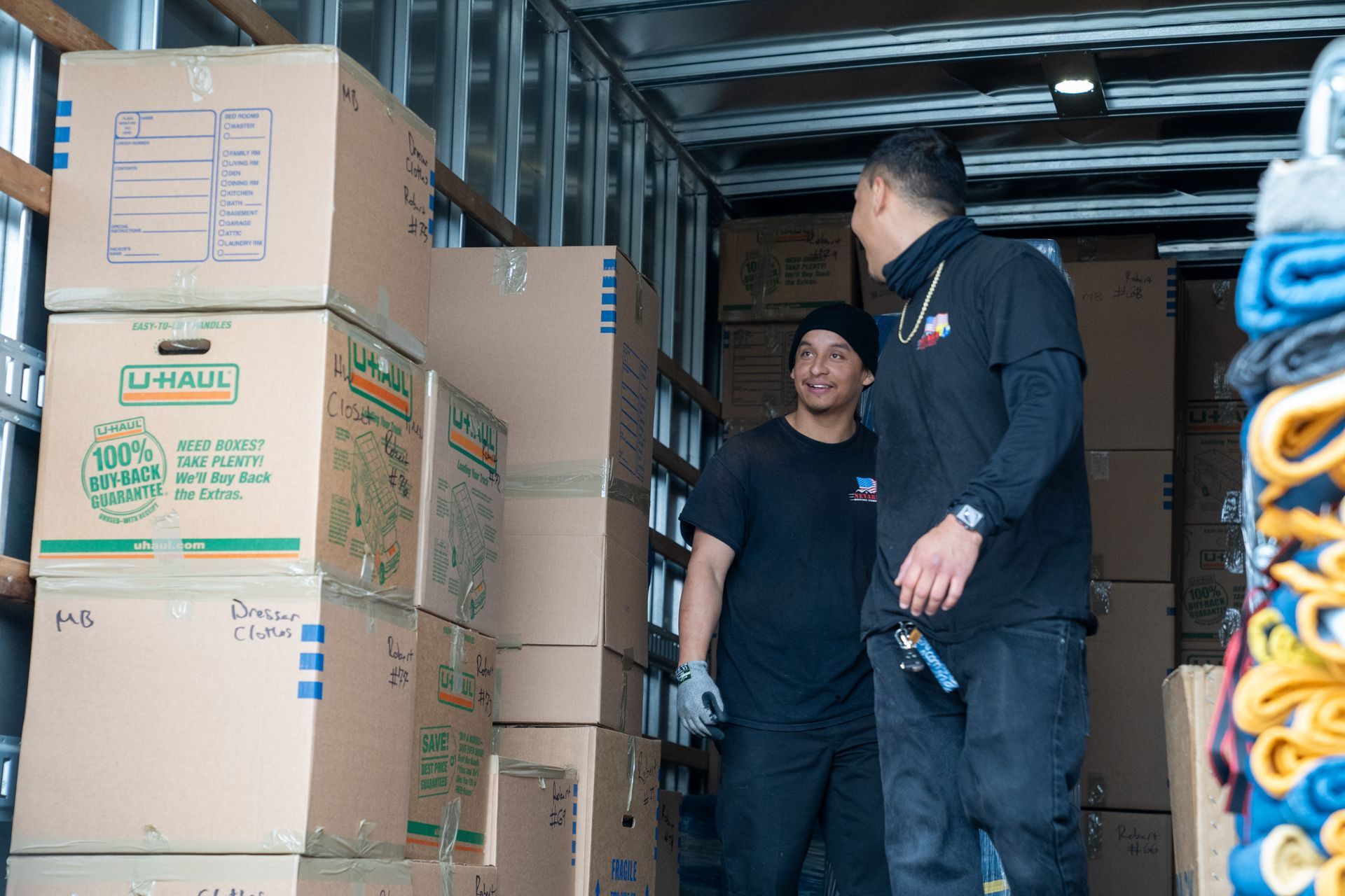 Two men are standing in a truck filled with boxes.