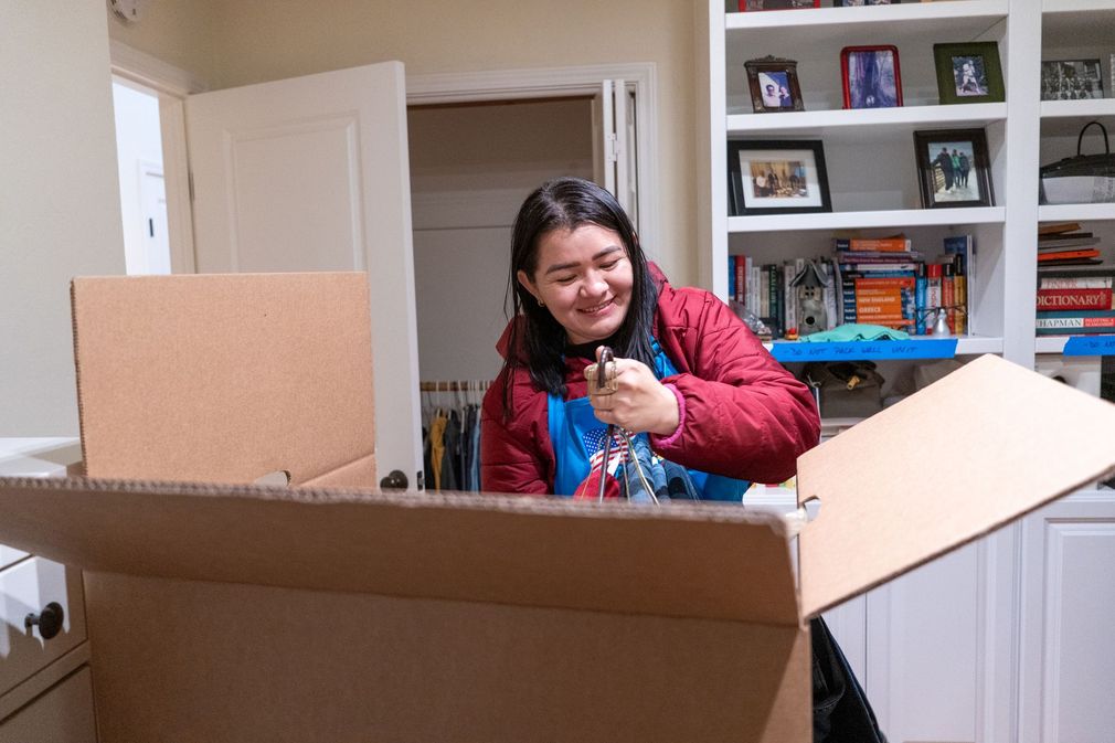 A woman is sitting in a cardboard box in a living room.