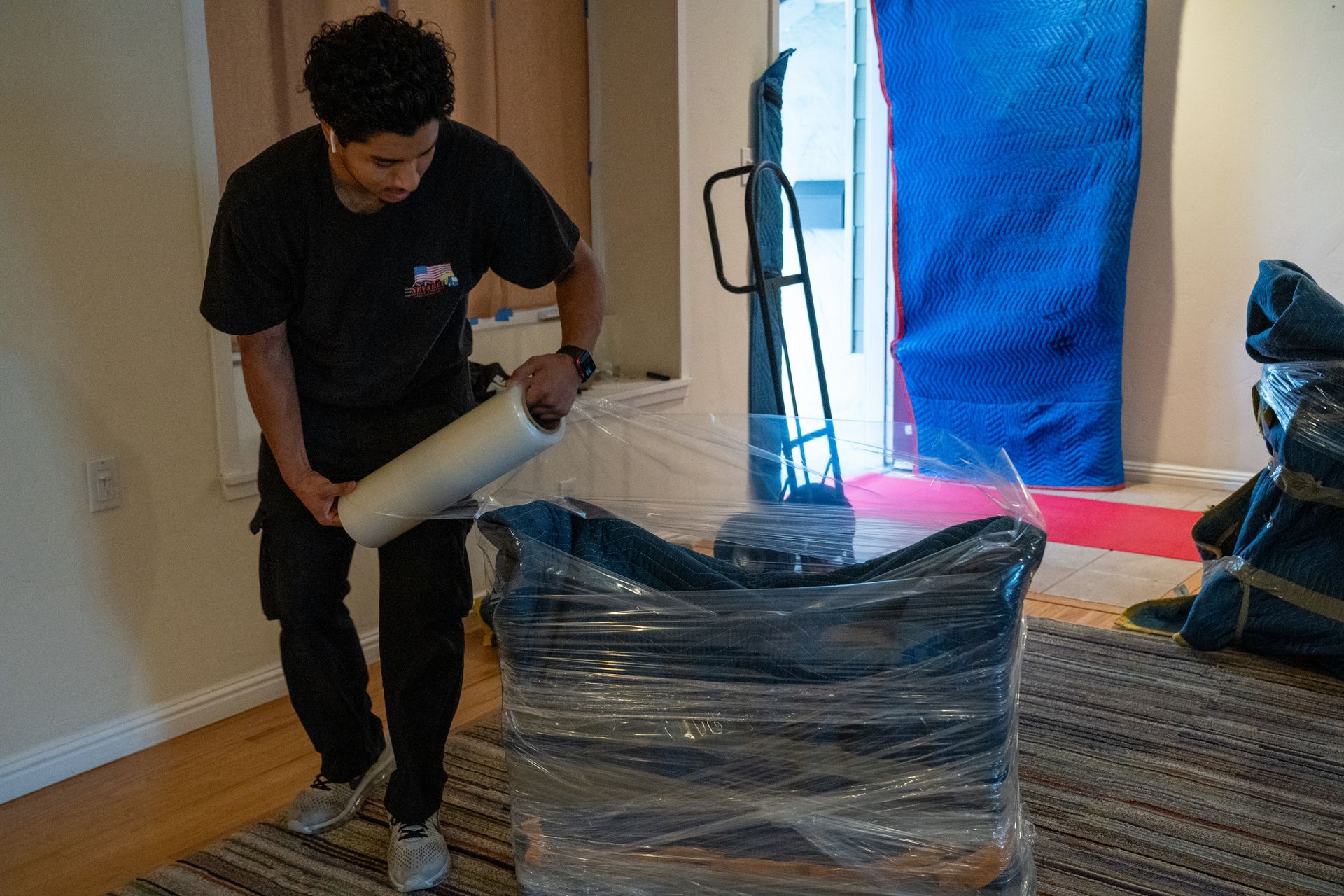 A man is wrapping a chair with plastic wrap in a living room.