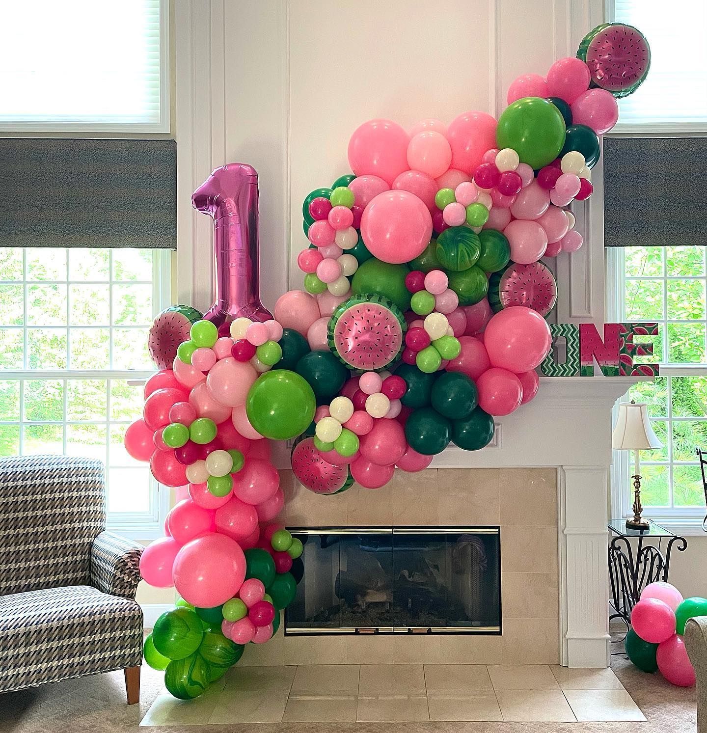 A fireplace decorated with pink and green balloons for a first birthday.