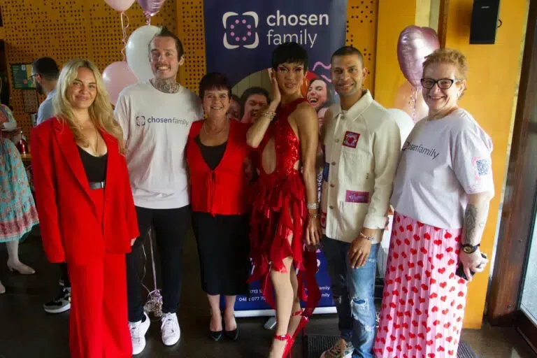 Group of people posing together, some in red attire, in front of a banner that says