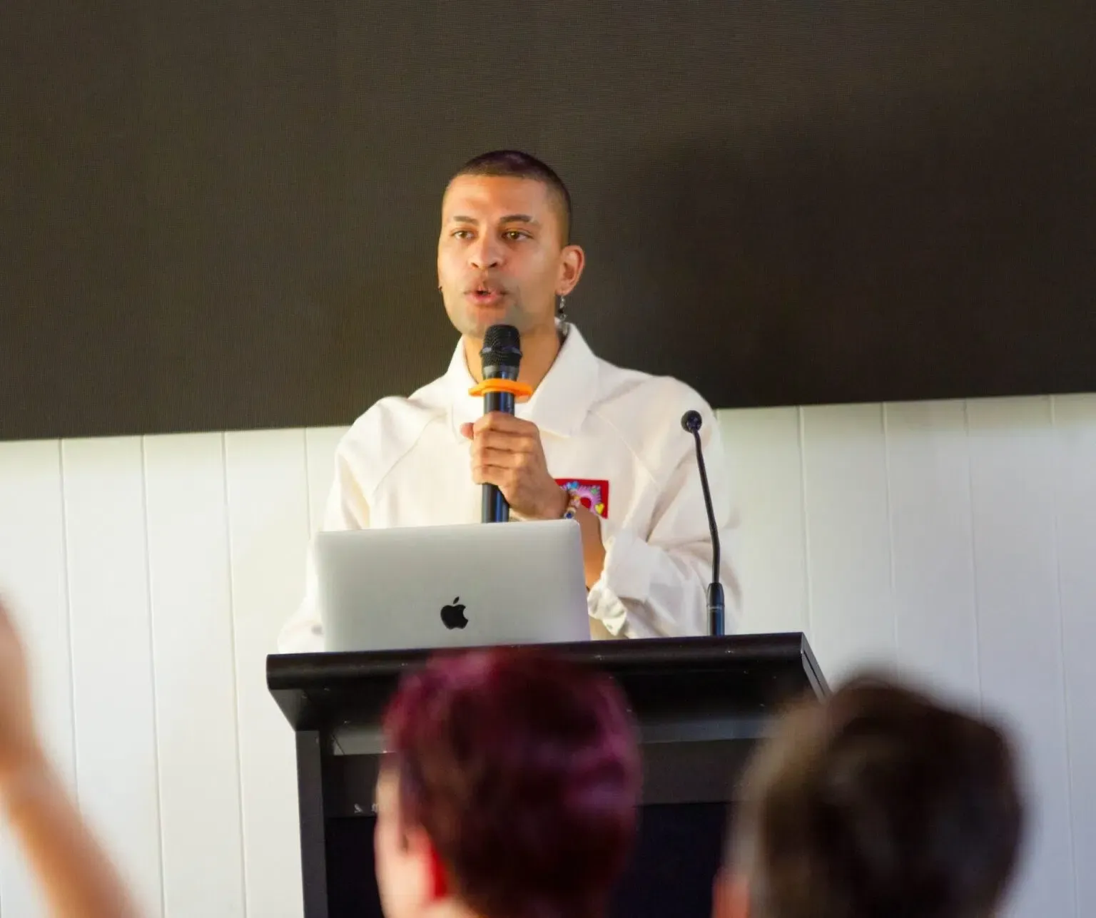 Man speaking at a podium, holding a microphone, with a laptop in front of him.