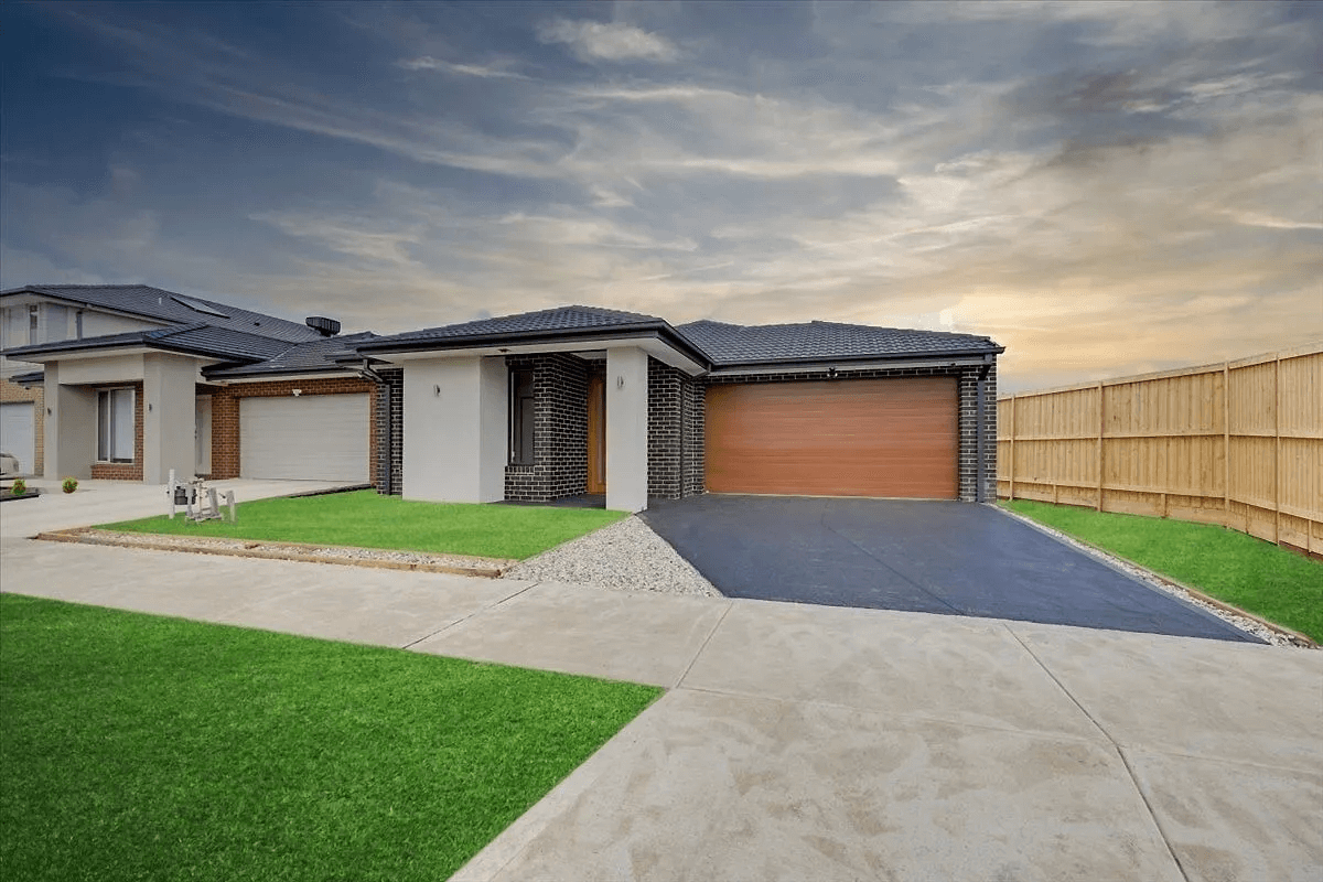 Modern home with a dark roof and a brown garage door, set on green grass and a concrete driveway.