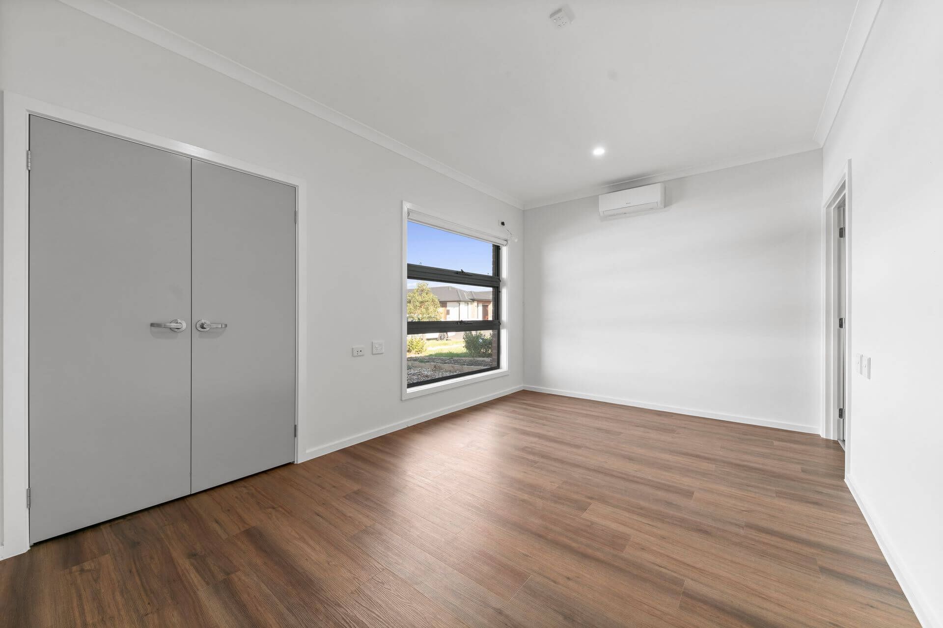 Empty room with wood floors, large grey closet doors, window, and air conditioner.