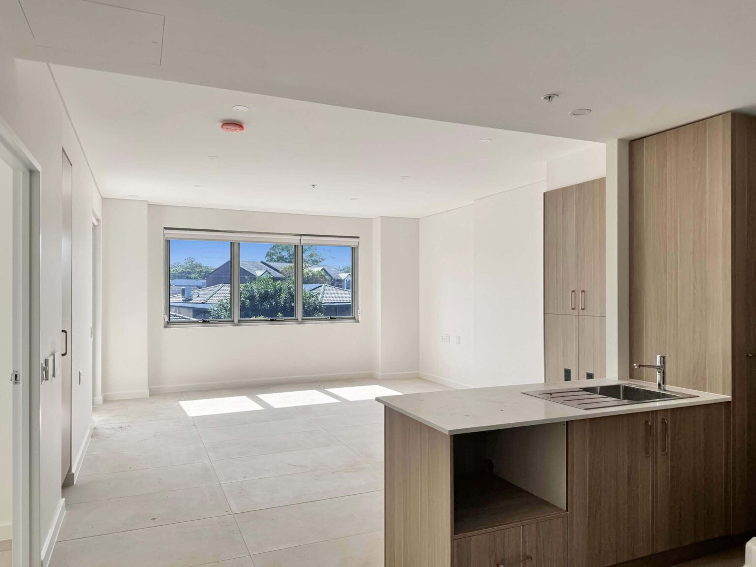 Empty apartment interior with a kitchen island, window, and cabinets; neutral colors.