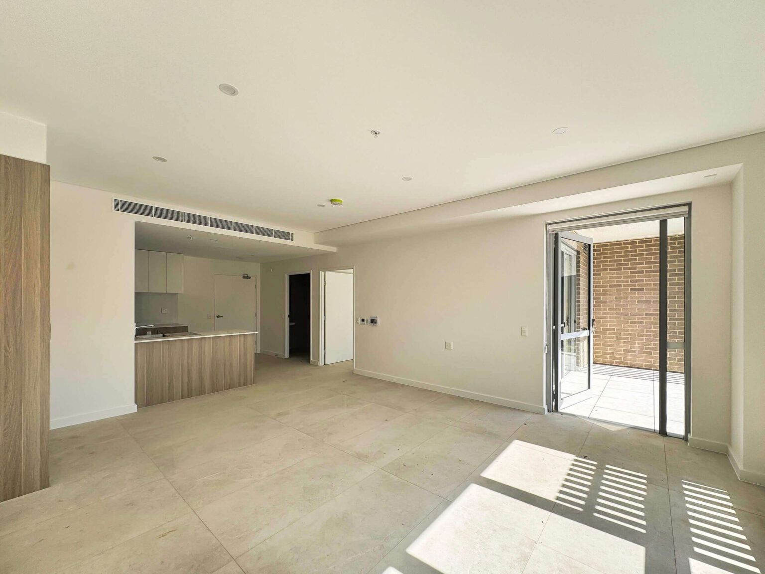Empty, bright apartment interior with balcony access. Kitchen island visible. Natural light.