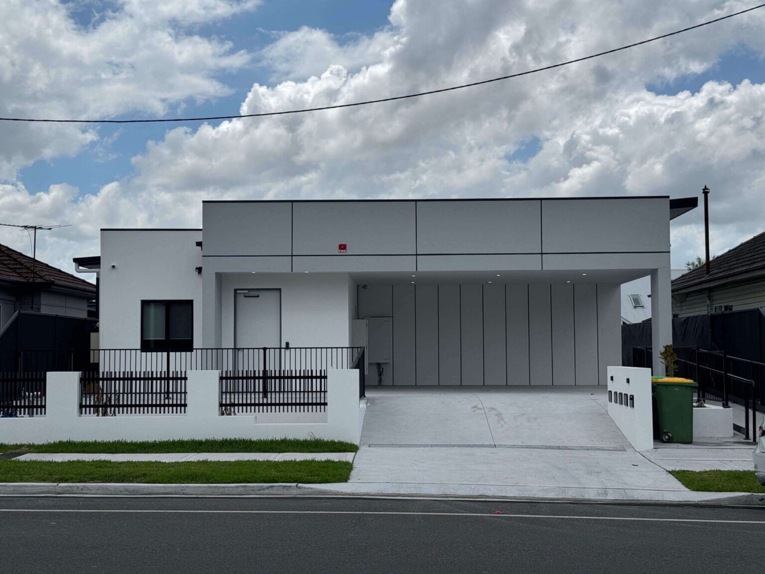 Modern white building with a covered carport, black fence, and driveway.