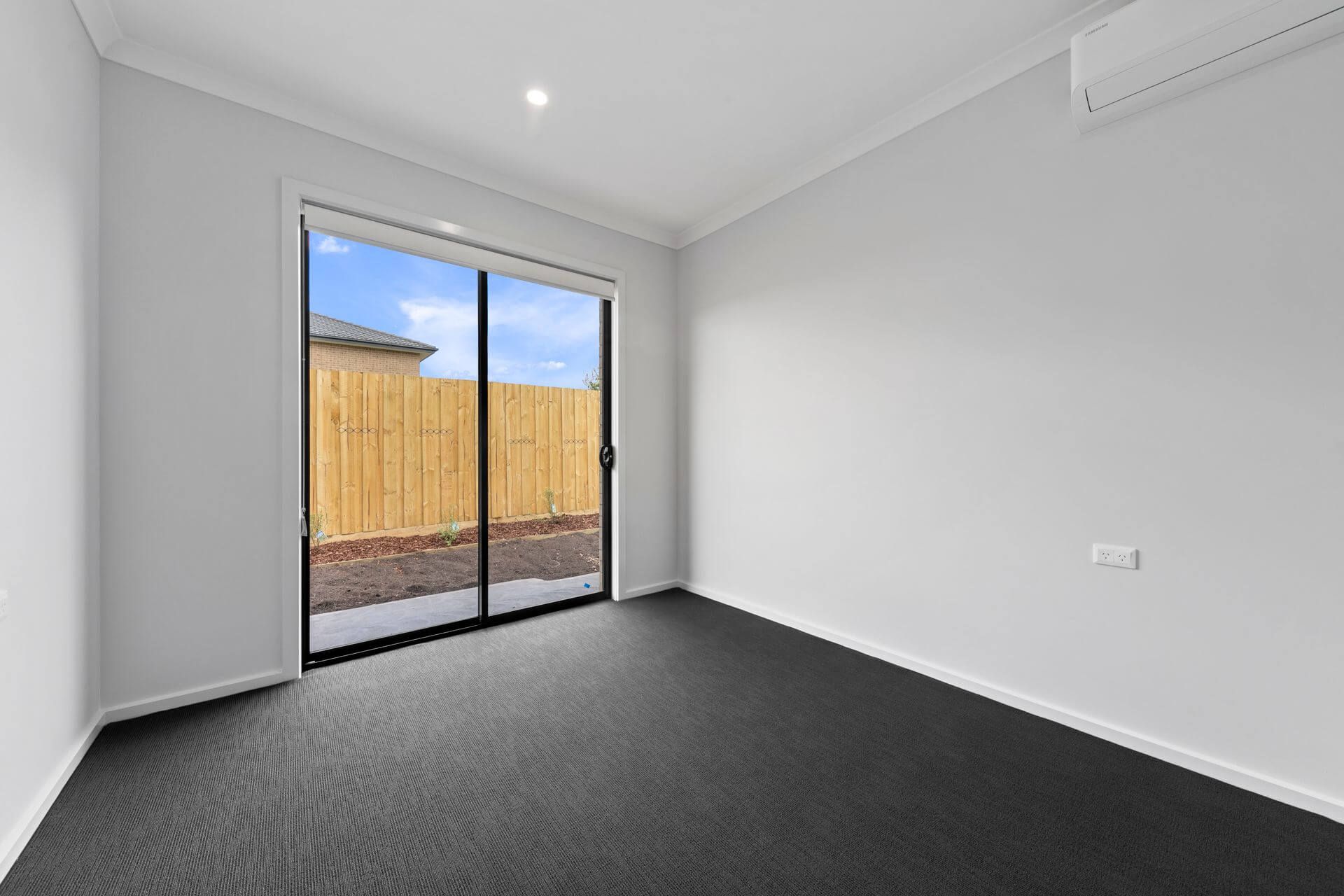 Empty room with sliding glass door and dark gray carpet, opening to a wooden fence.