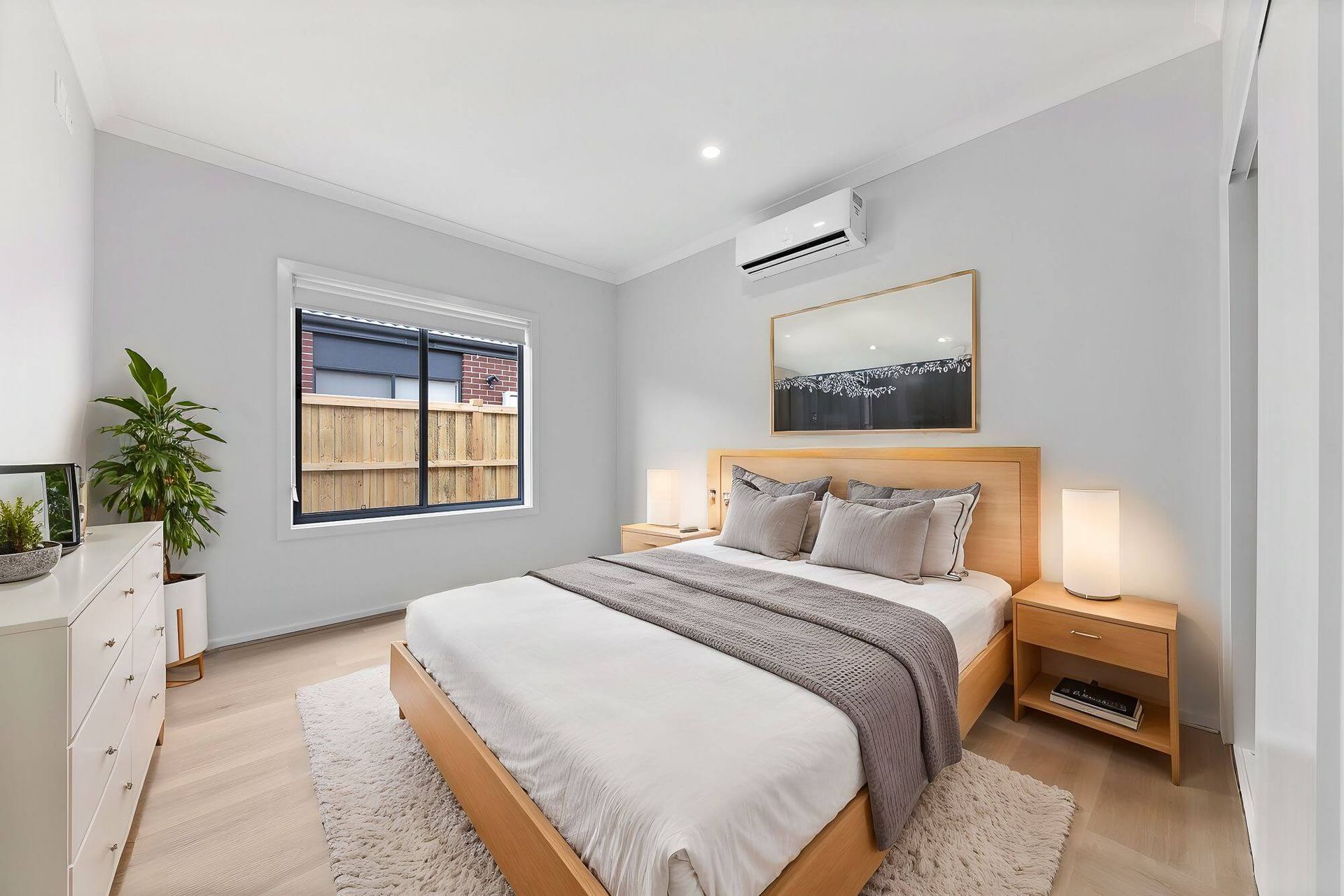Bedroom with a wooden bed frame, bedside tables, and a dresser. Features a window, artwork, and a rug.