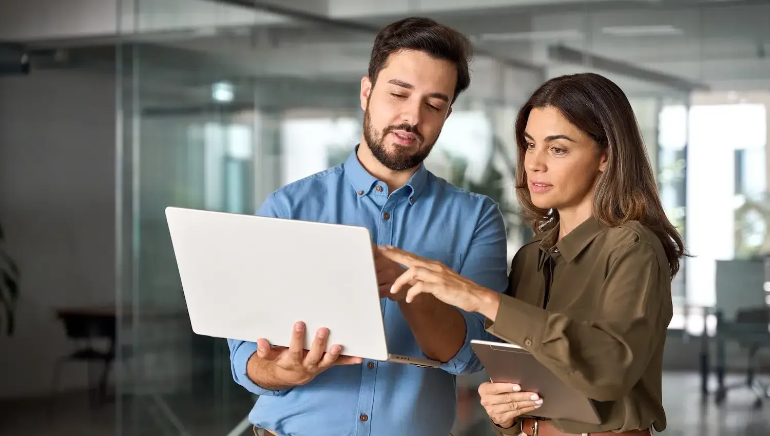 Man and woman reviewing laptop together, pointing to the screen in office setting.