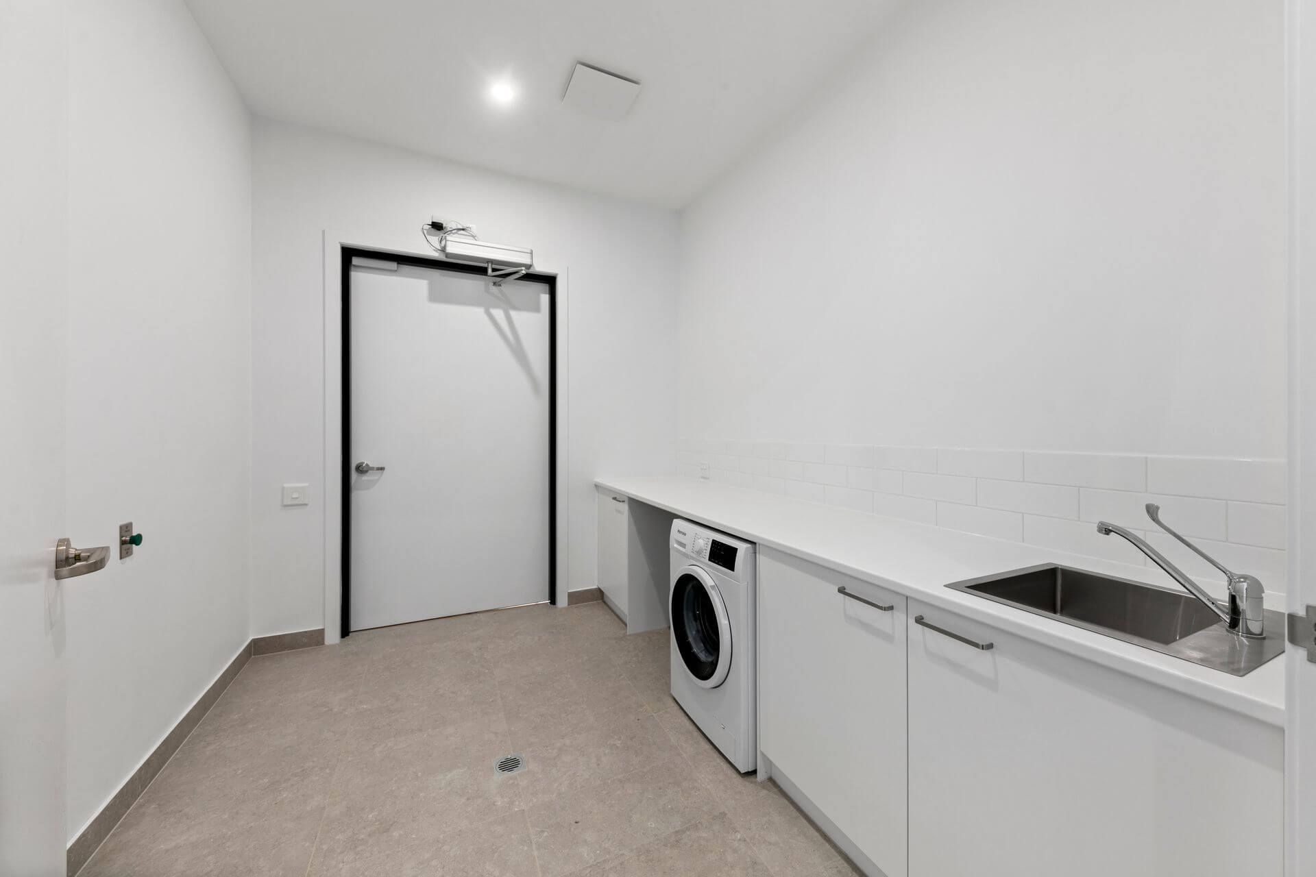 Laundry room with white cabinets, countertop, and appliances. Door on the left.