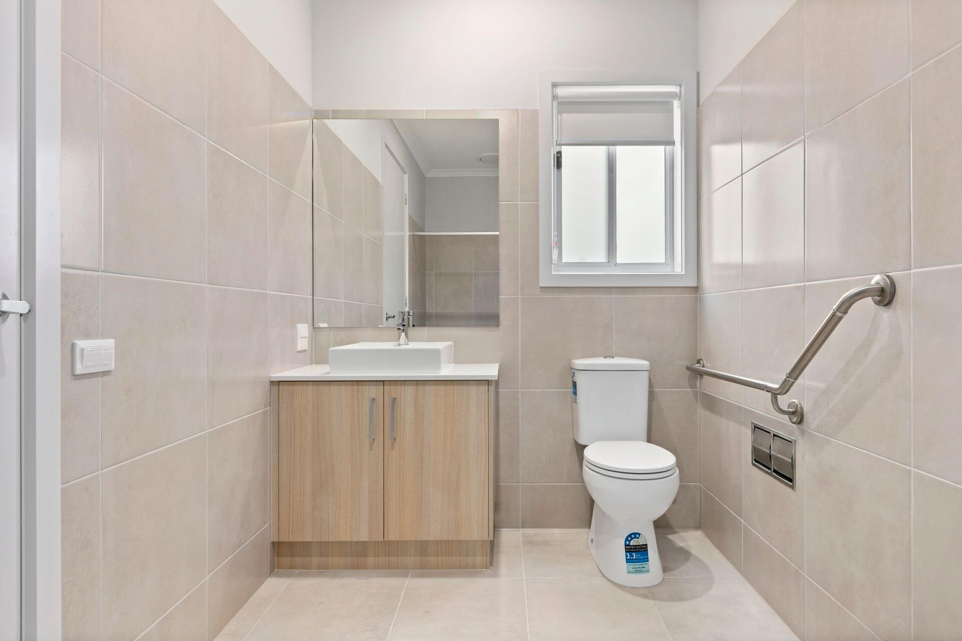 Accessible bathroom with beige tiling, a vanity, toilet with grab bar, and a window.
