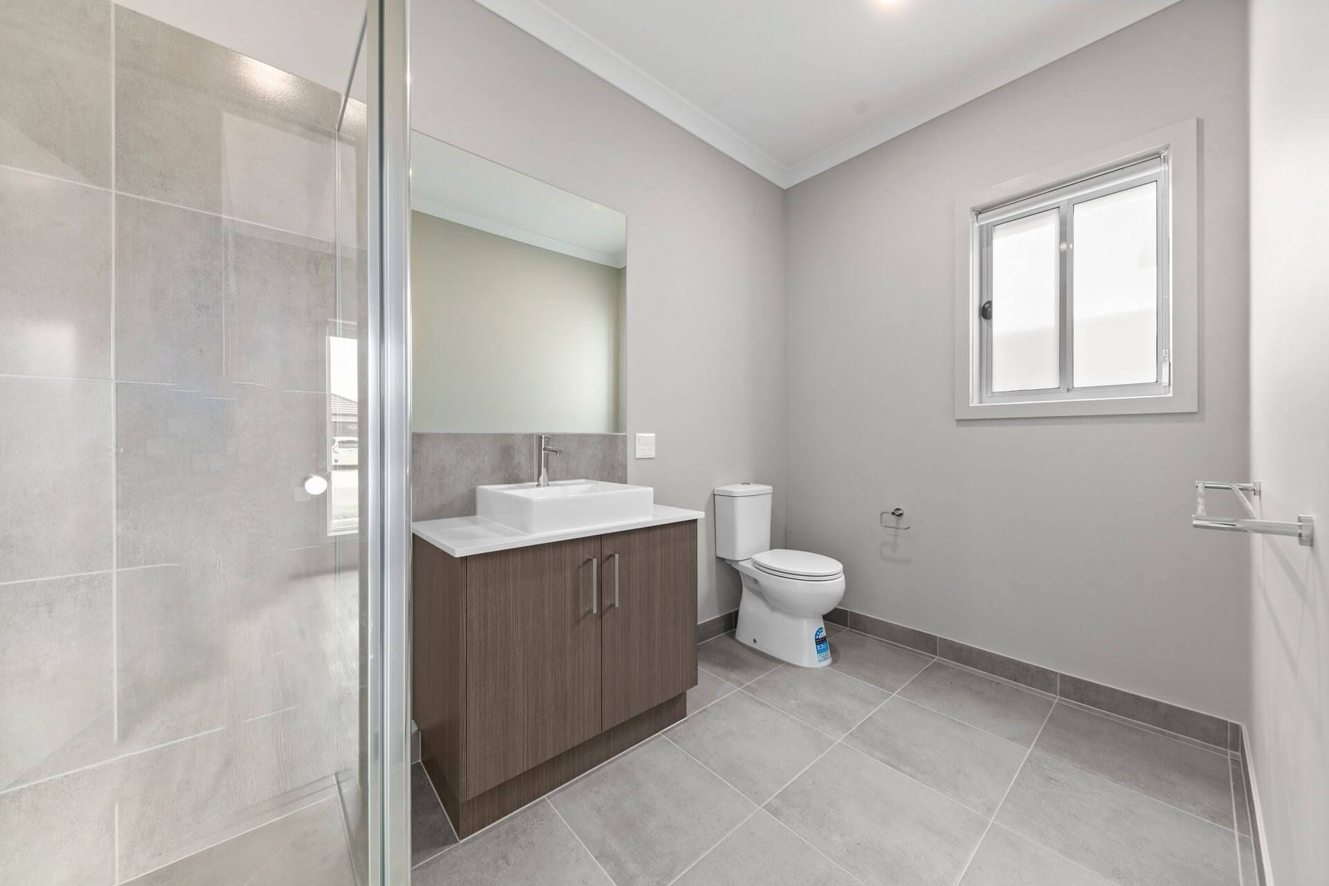 Bathroom with gray tile, shower, vanity, toilet, and window.