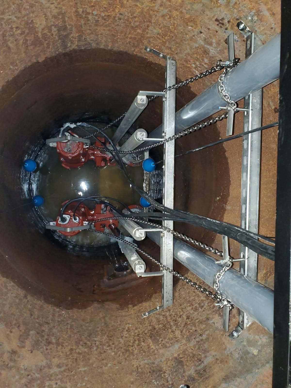 Inside a rusty pipe, a wet mechanical assembly with red fittings and gray pipes is being inspected.