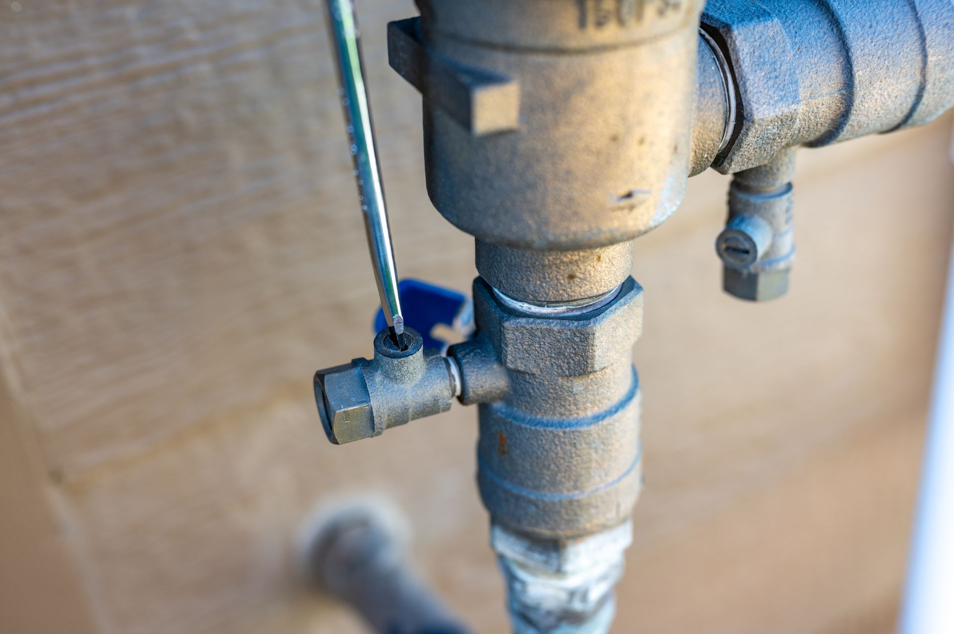 Close-up of a metal pipe valve with a blue handle on a blurred industrial background