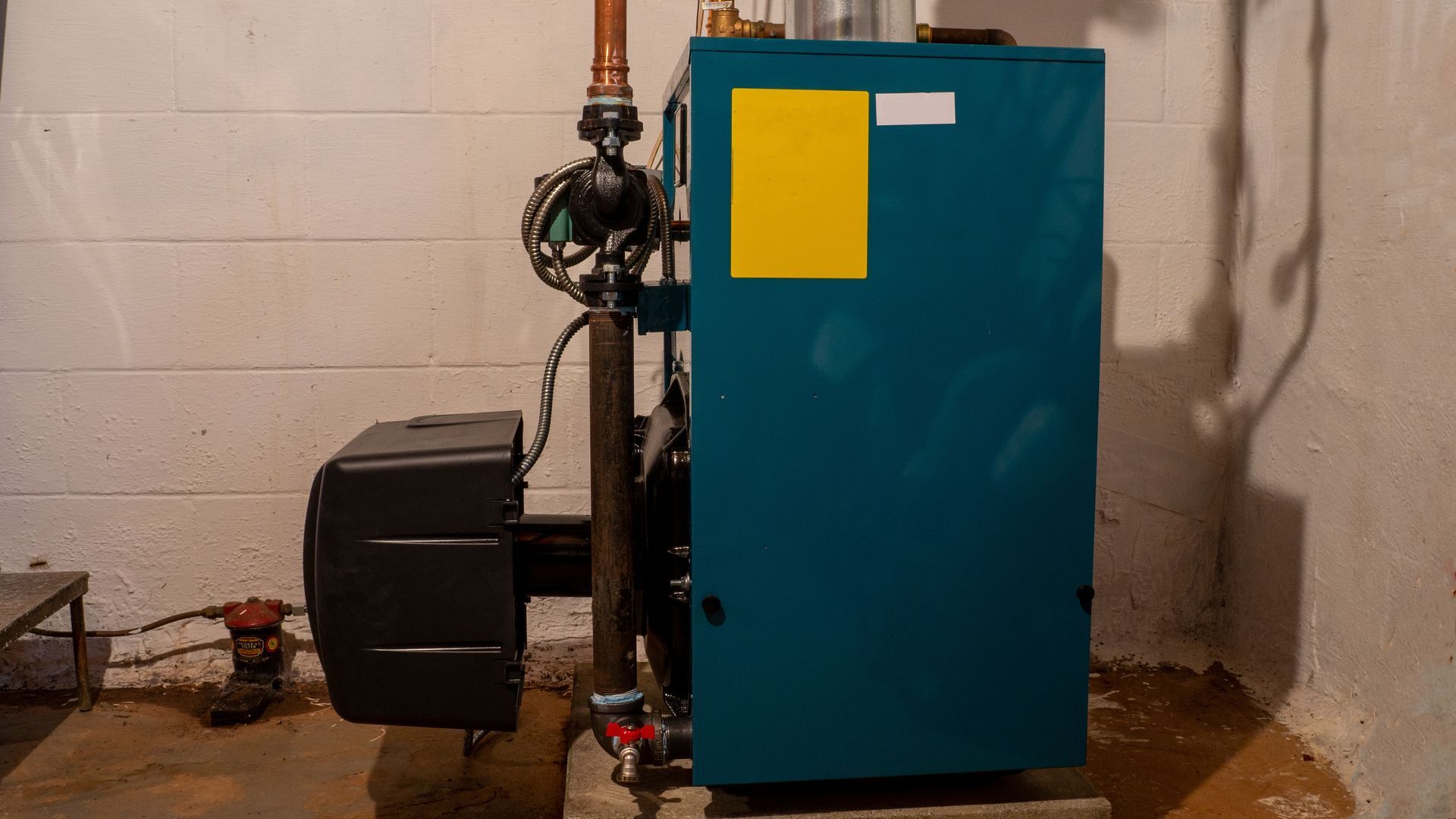 Blue industrial boiler unit with pipes and a black tank in a utility room