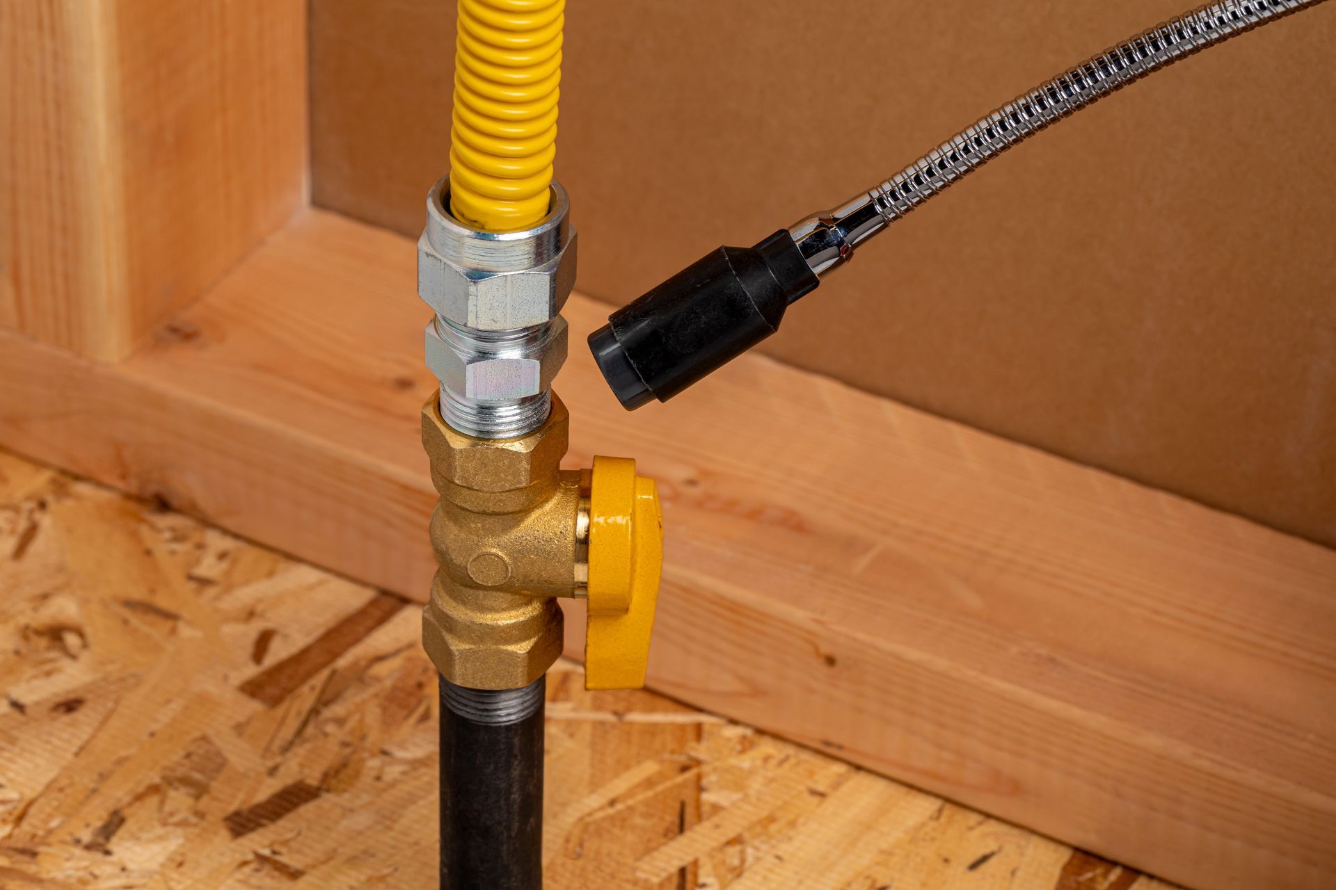 Yellow gas line with shutoff valve and black pipe connection on a wooden floor.