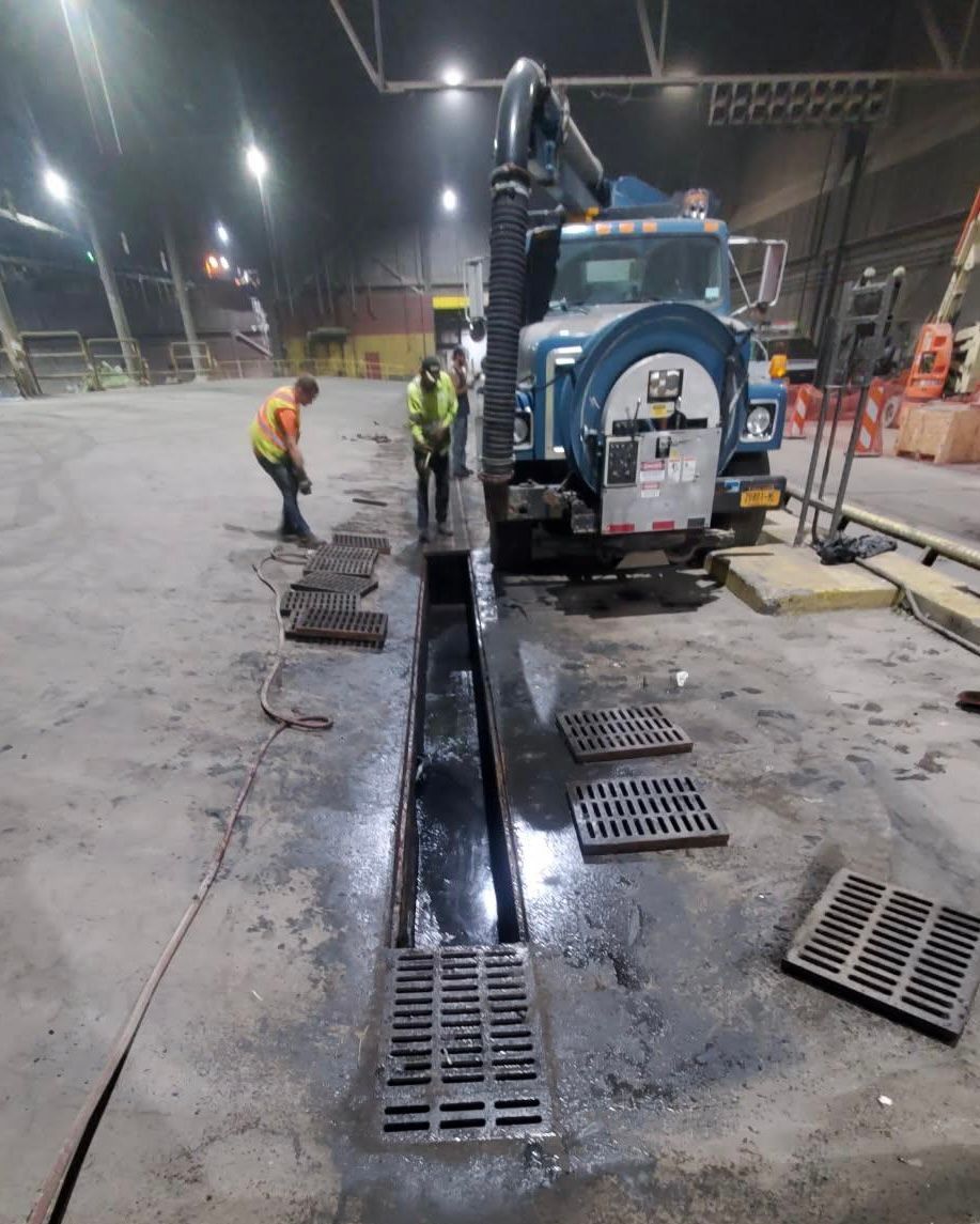 Workers inspecting a trench drain beside a blue utility vehicle on a wet night construction site