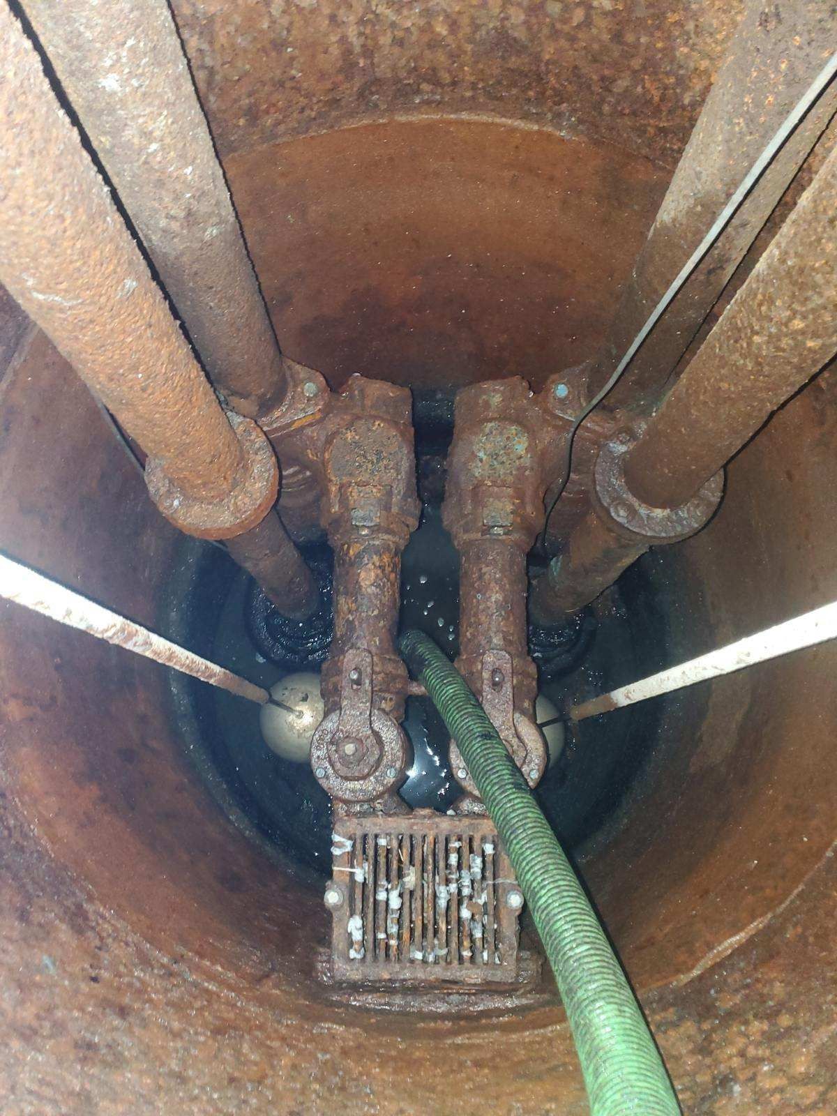 Rusty industrial pipe assembly inside a tank, with a green hose connected to a valve.