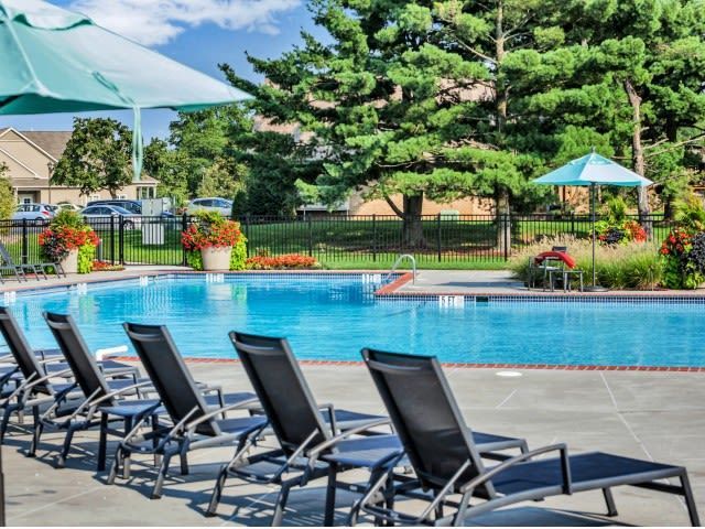 Outdoor apartment community pool with lounge chairs and umbrellas.
